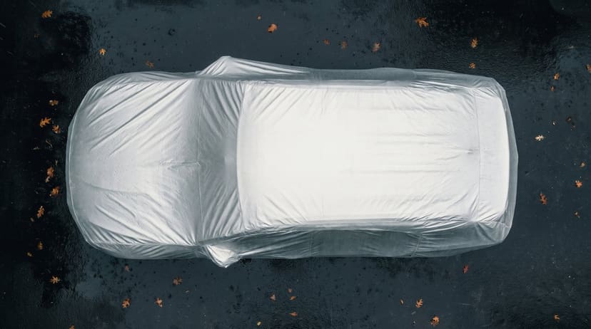 Top-down view of a silver reflective cover fitted over an SUV on dark wet pavement with a few fallen leaves.