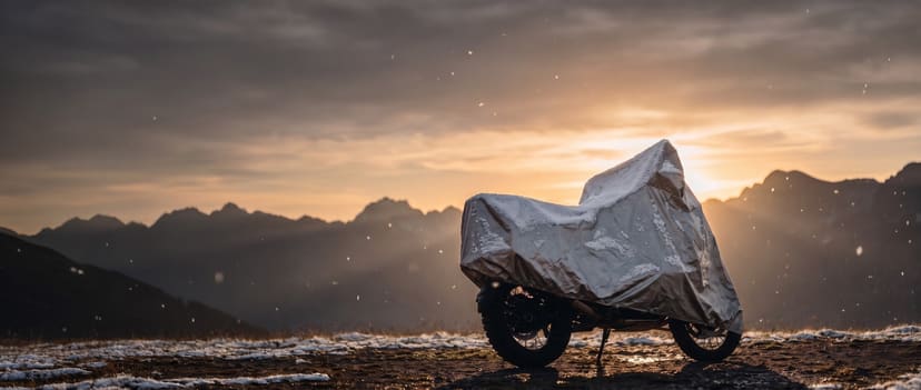 Silver cover on an adventure motorcycle dusted with snow on a mountain ridge at sunset