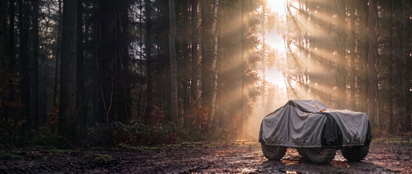 Grey and black cover cinched under the body with an elastic hem on a quad bike on a misty forest track at sunrise