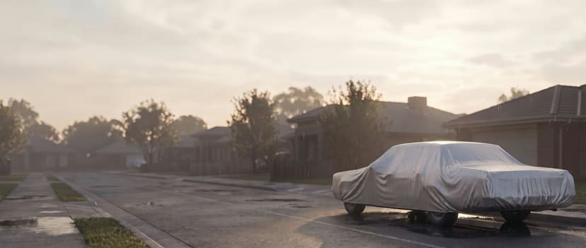 Silver cover on a full-size sedan beaded with rain on a quiet suburban street at sunrise