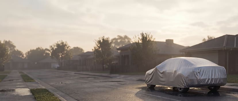 Silver cover on a midsize sedan after rain at a wet suburban kerb at sunrise