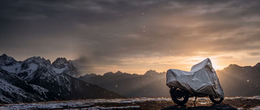 Silver cover on an adventure motorcycle dusted with snow on a mountain ridge at sunset