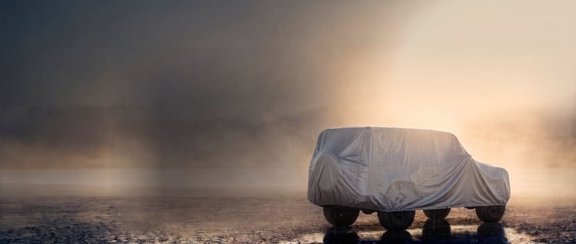 Silver cover on a boxy off-road SUV beaded with light rain on wet ground