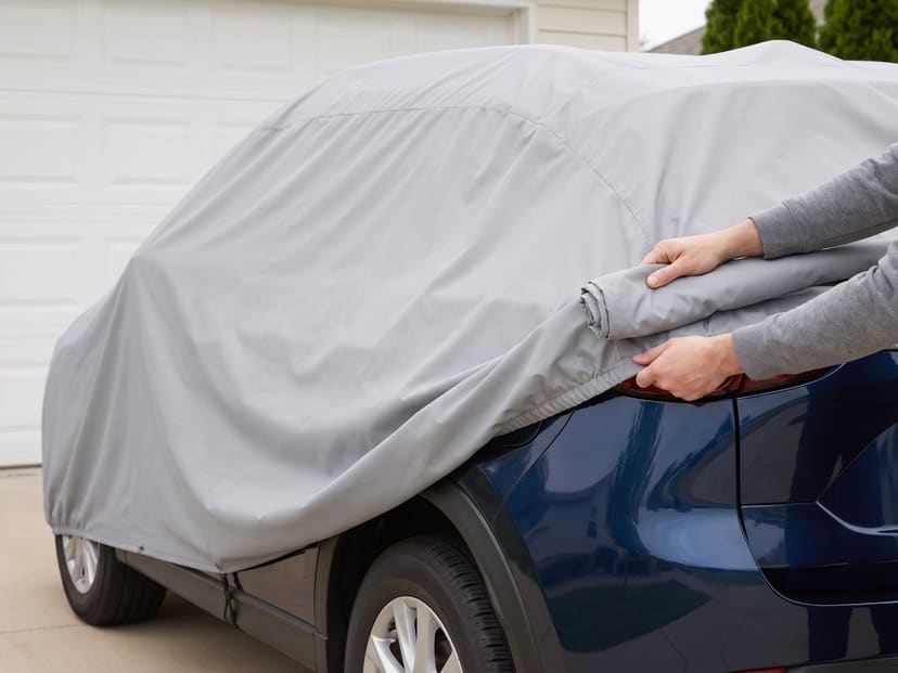 Hands rolling a light grey cover forward off the back of a dark blue SUV in front of a garage door