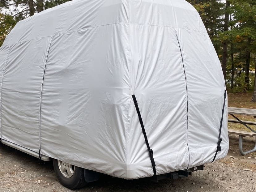 The rear of a Class B camper van beside a lake, under a fitted silver cover.