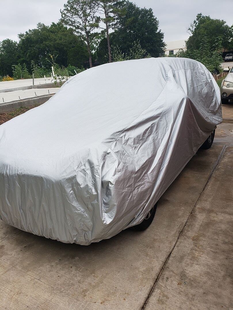 A customer's SUV under a silver cover on a concrete driveway.