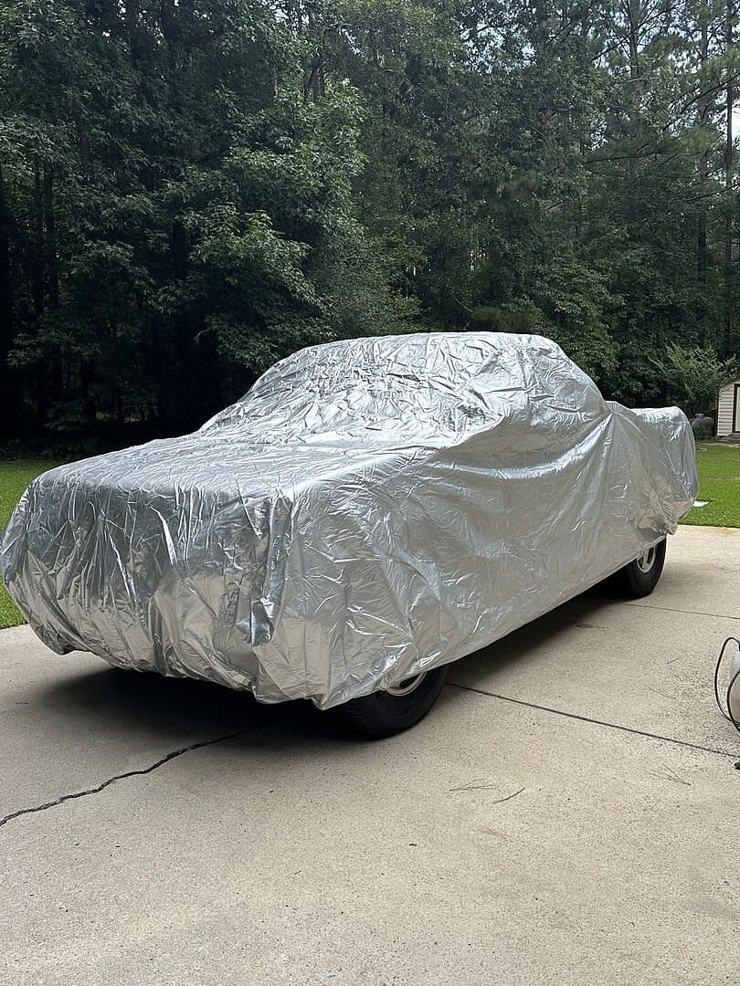 A customer's pickup under a silver cover on a concrete driveway, trees behind it.