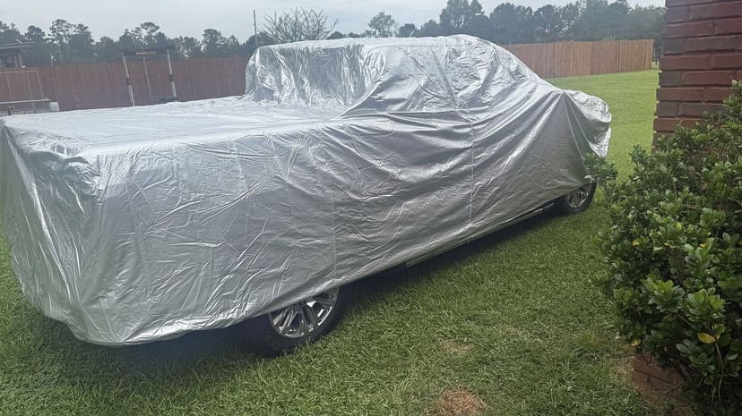 A customer's pickup under a silver cover parked on a lawn beside a hedge.