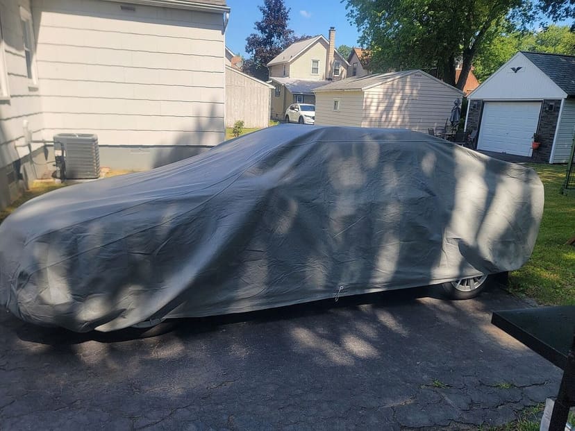 Owner photo from Justin E.: a sedan under a light grey cover on a driveway in dappled shade