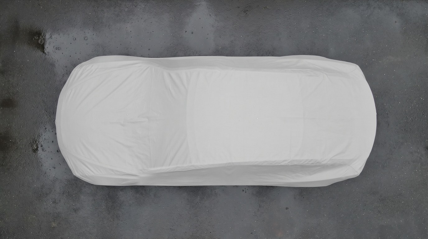 Top-down view of a sedan under a matte light grey cover on dark wet pavement.