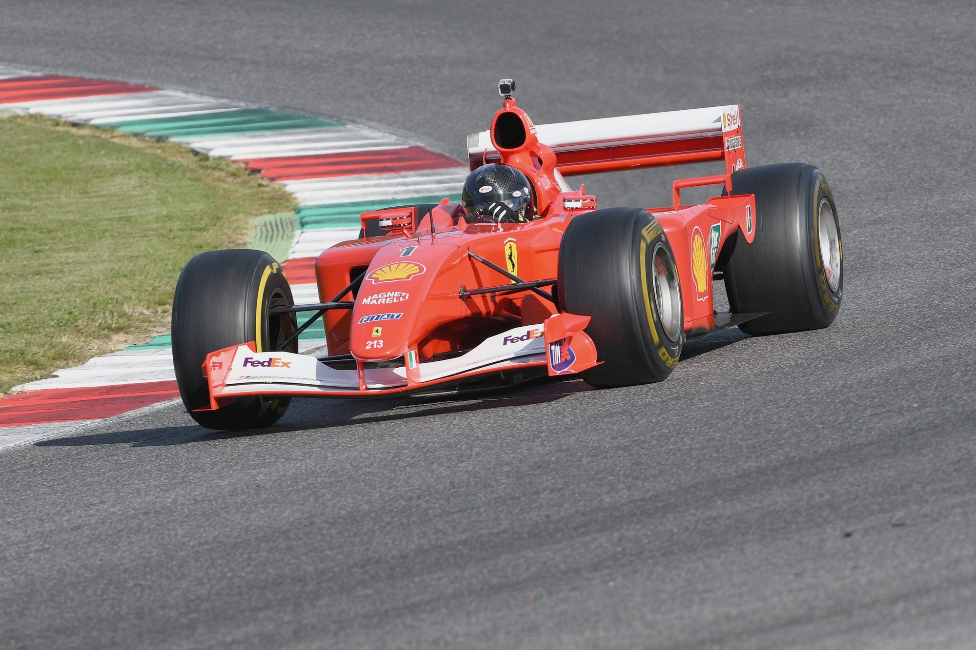 A red Ferrari Formula 1 car from the early 2000s, number 1 on its nose, cornering past red, white and green curbs at a race circuit