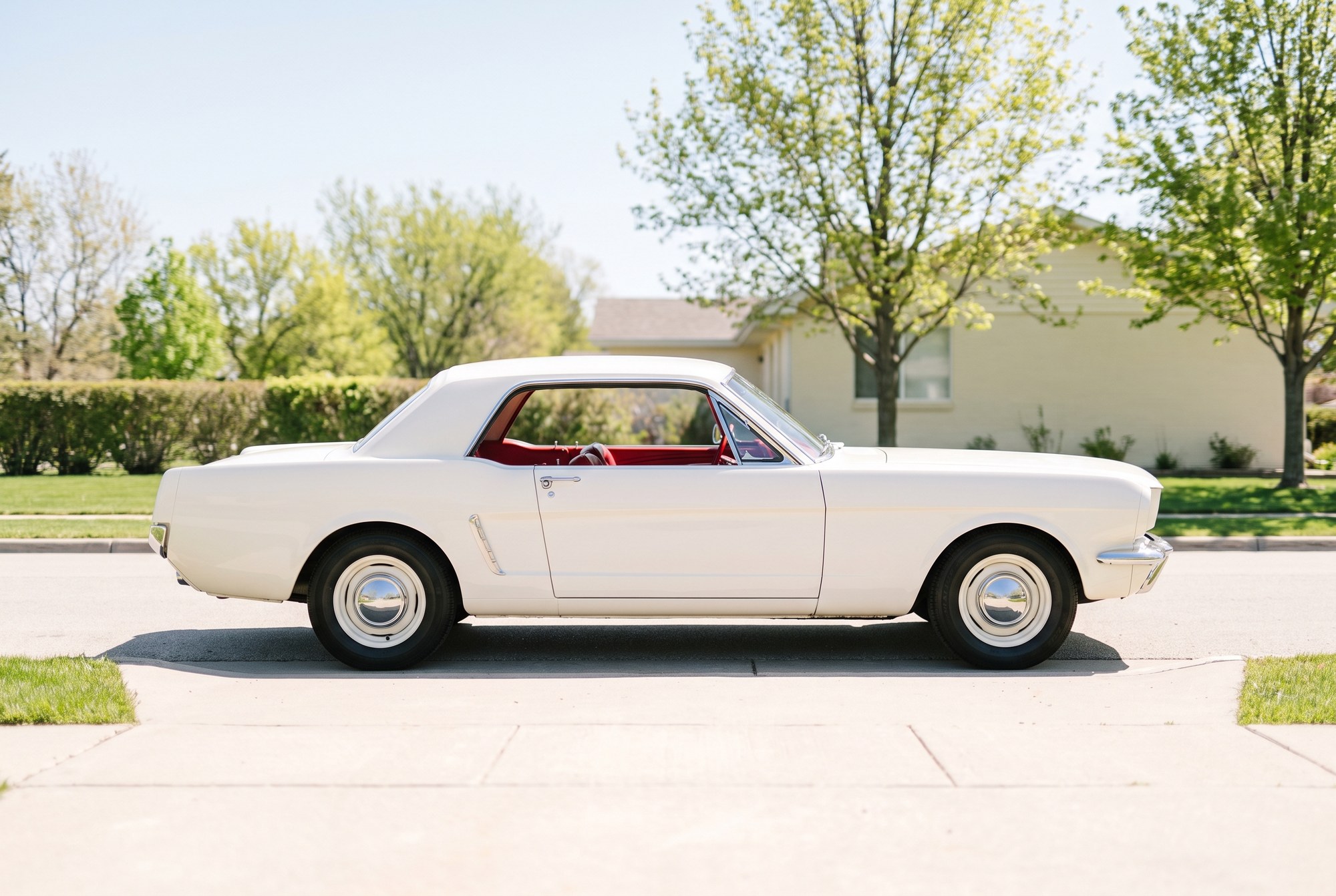 An AI illustration of a white 1965 Ford Mustang hardtop coupe with a red interior, in profile on a sunny residential street with leafy trees and a house behind it
