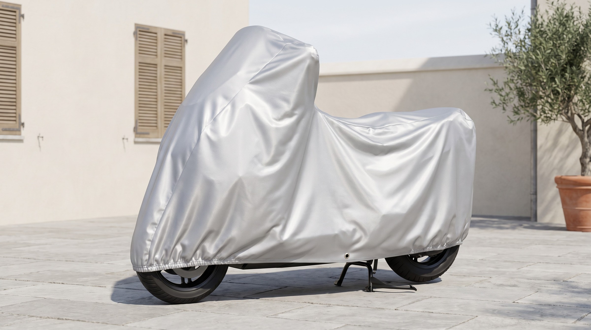 A scooter under a bright silver cover on a pale stone courtyard.