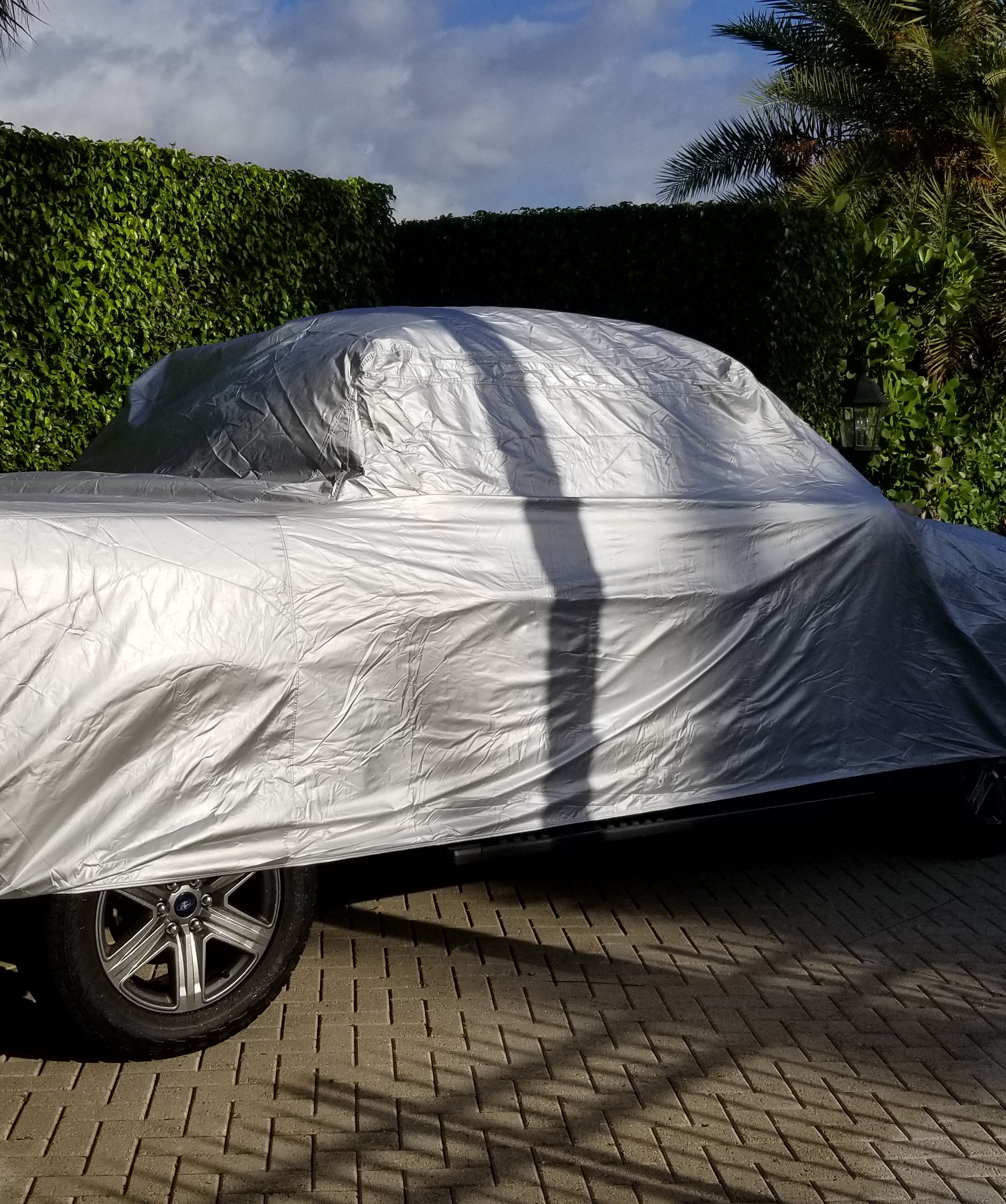 A Ford F-150 SuperCrew in a driveway under a silver outdoor cover, the cab-to-bed step and roofline reading through the fabric