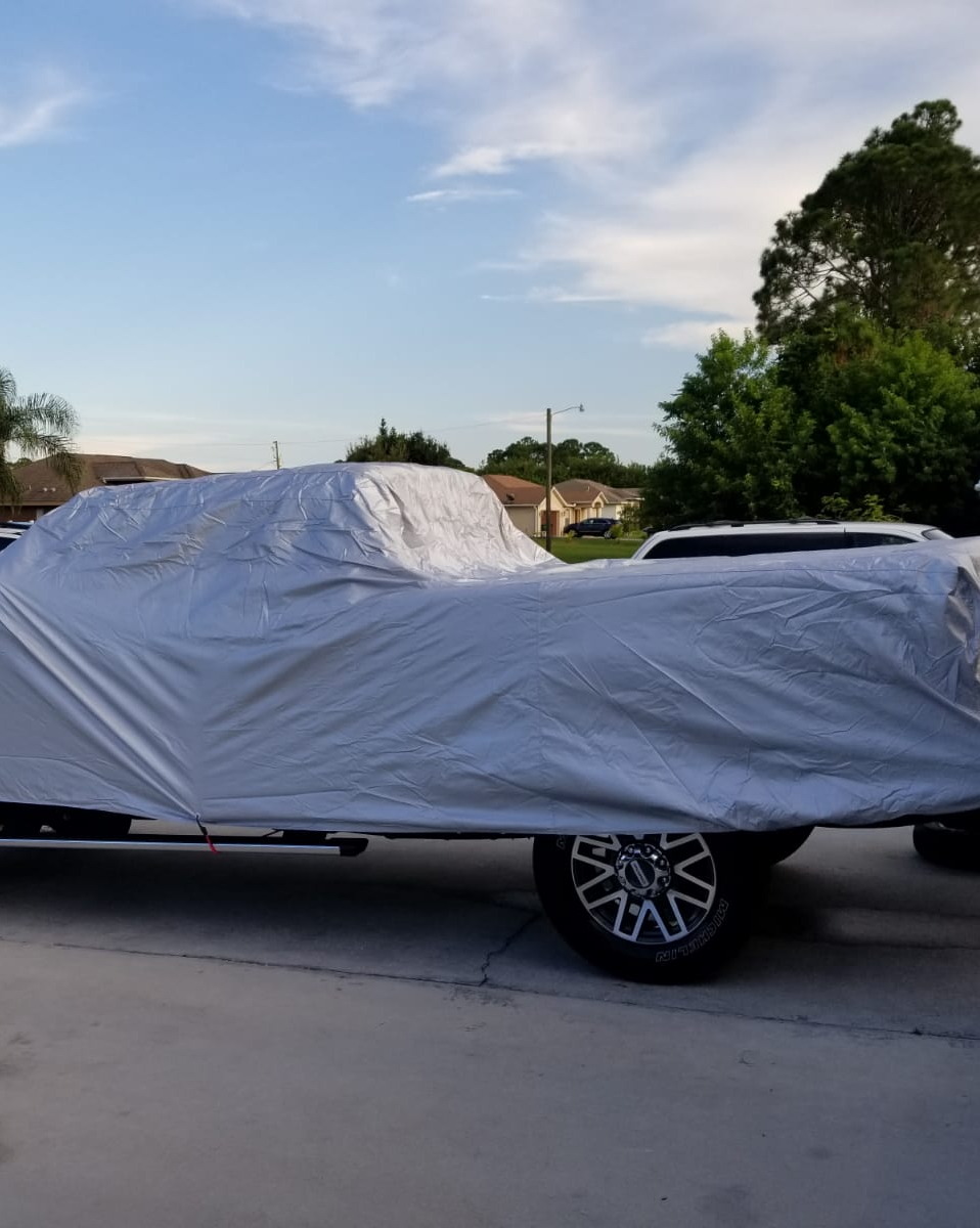 A silver outdoor cover over the cab and bed of a Ford F-250 Super Duty in a driveway, one continuous piece from the A-pillar back