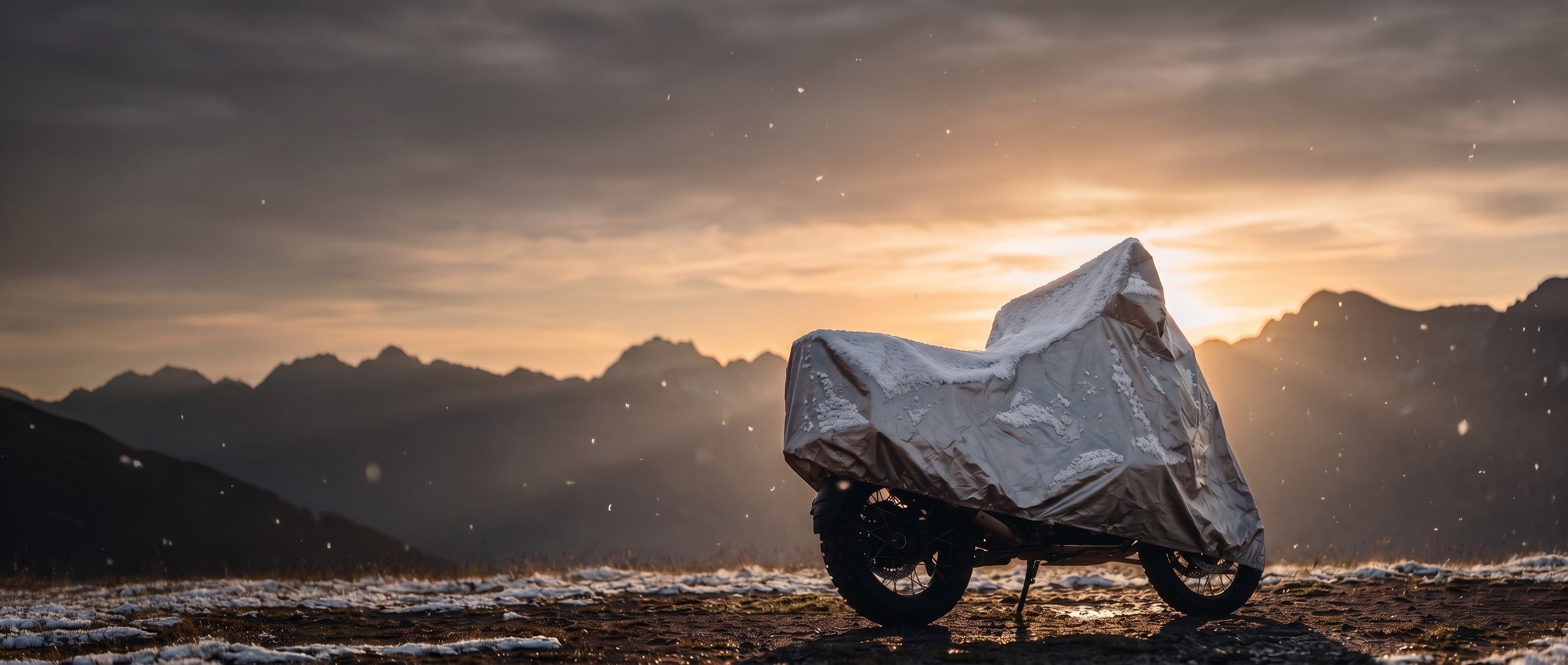 Silver cover on an adventure motorcycle dusted with snow on a mountain ridge at sunset