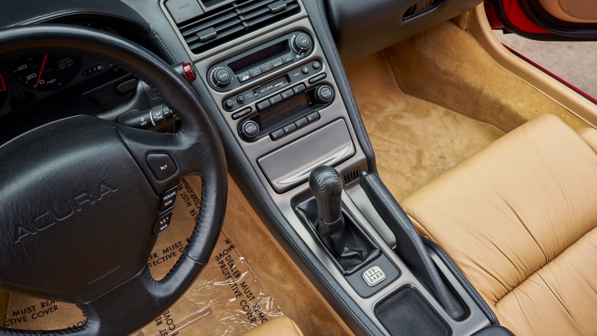 The NSX's center console from above: climate controls, an Acura Bose stereo and a leather-booted shifter with a six-speed shift pattern plate, beside a tan leather seat.