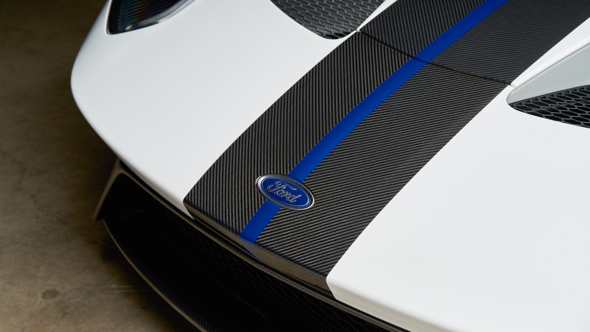 Close-up of the Ford GT's white nose with an exposed carbon fiber center stripe, a thin blue line and a Ford oval badge