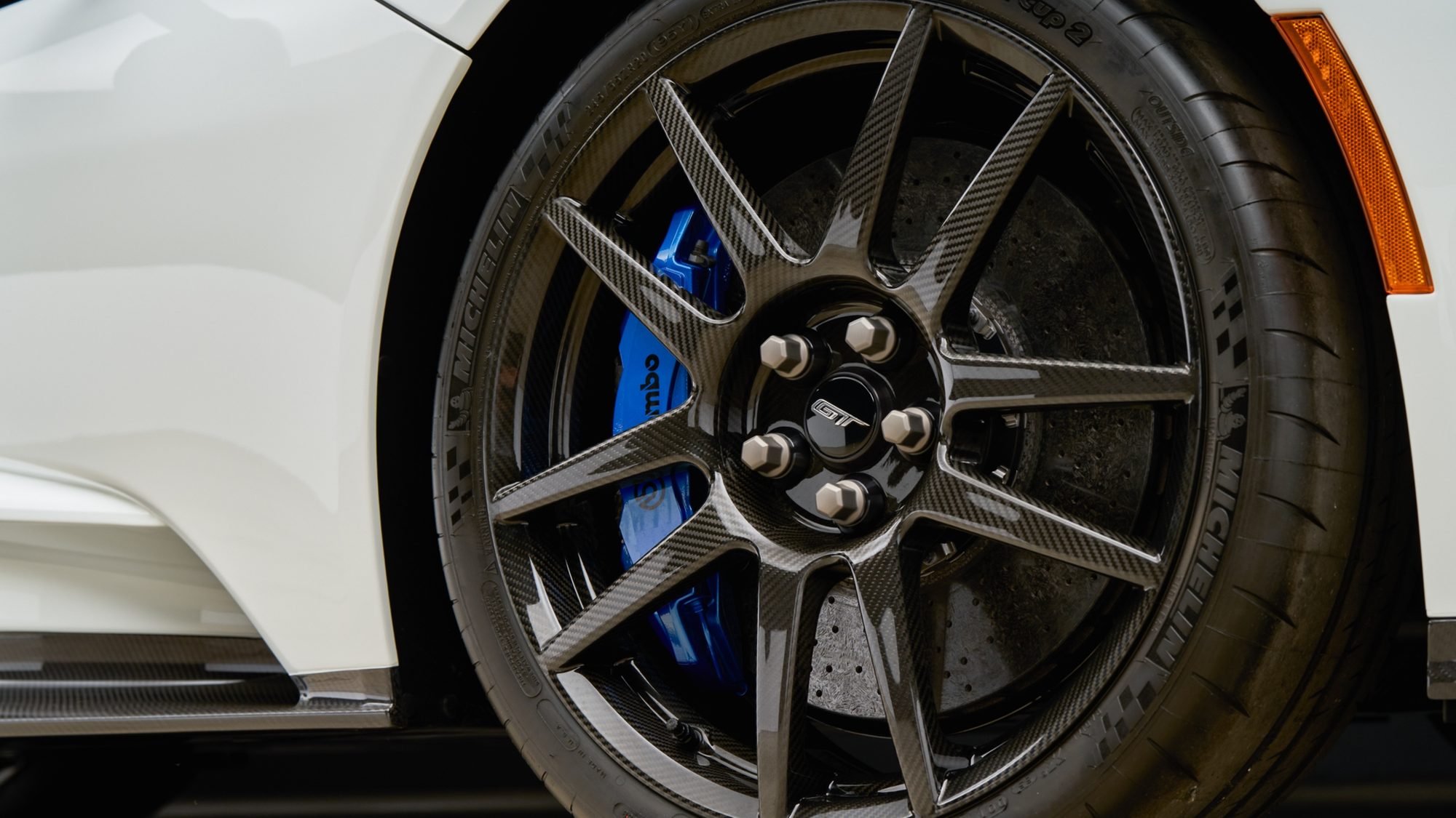 Close-up of a Ford GT carbon fiber wheel with a GT center cap, a blue Brembo brake caliper and a drilled brake rotor behind the spokes, on a Michelin tire
