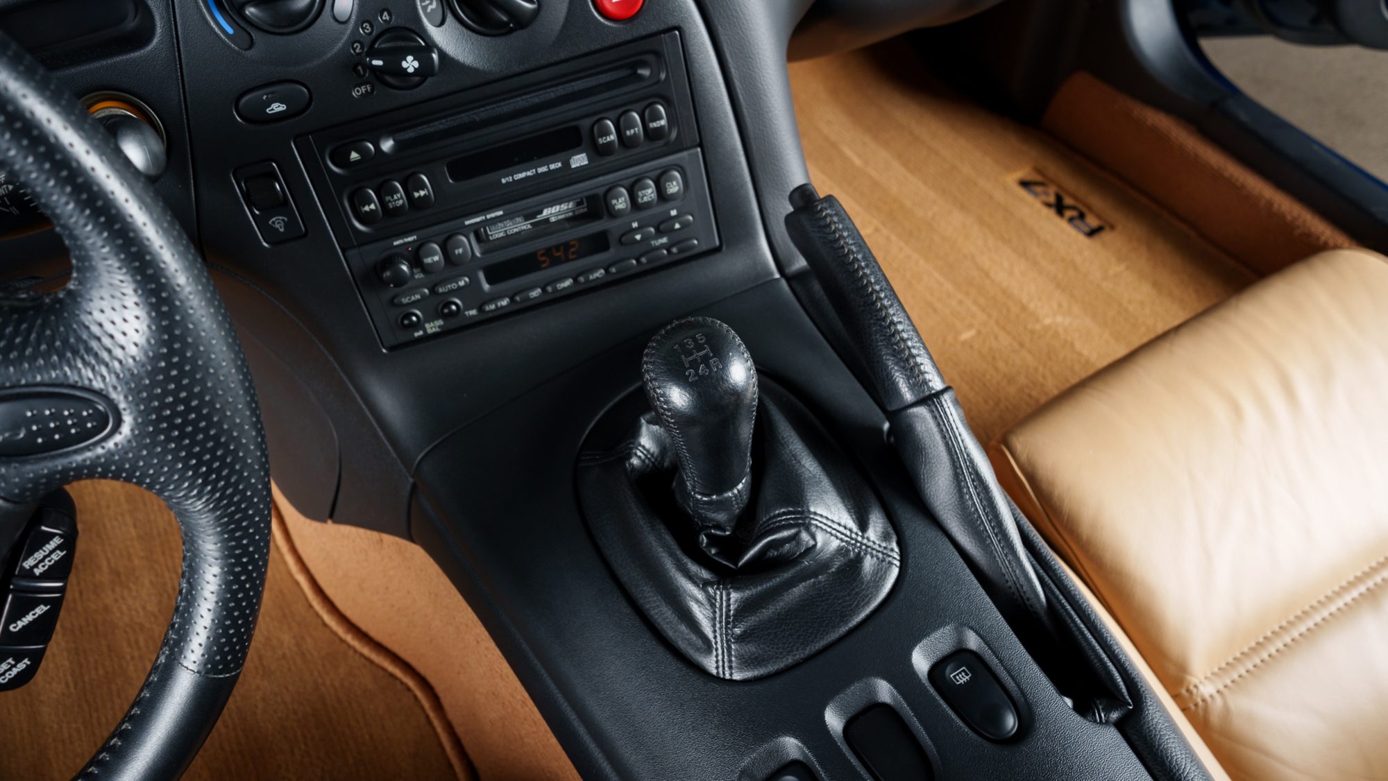 A close view of the RX-7 FD's center console, showing the leather-booted 5-speed shifter, the handbrake, a Bose CD and cassette stereo, and an RX-7 logo on the tan floor mat
