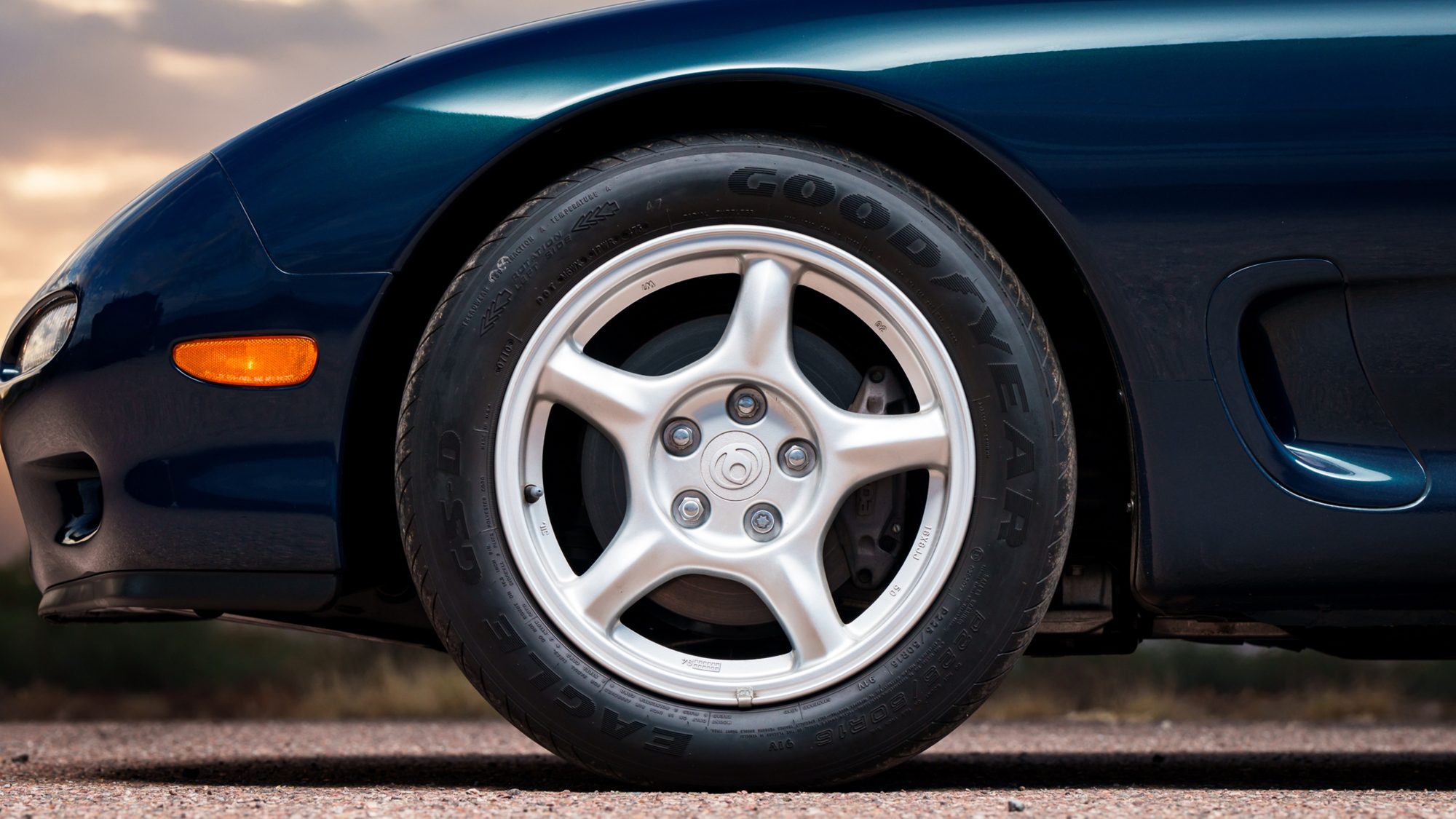 A close view of the Mazda RX-7 FD's front wheel and fender, showing its five-spoke alloy wheel, Goodyear tire and amber side marker light
