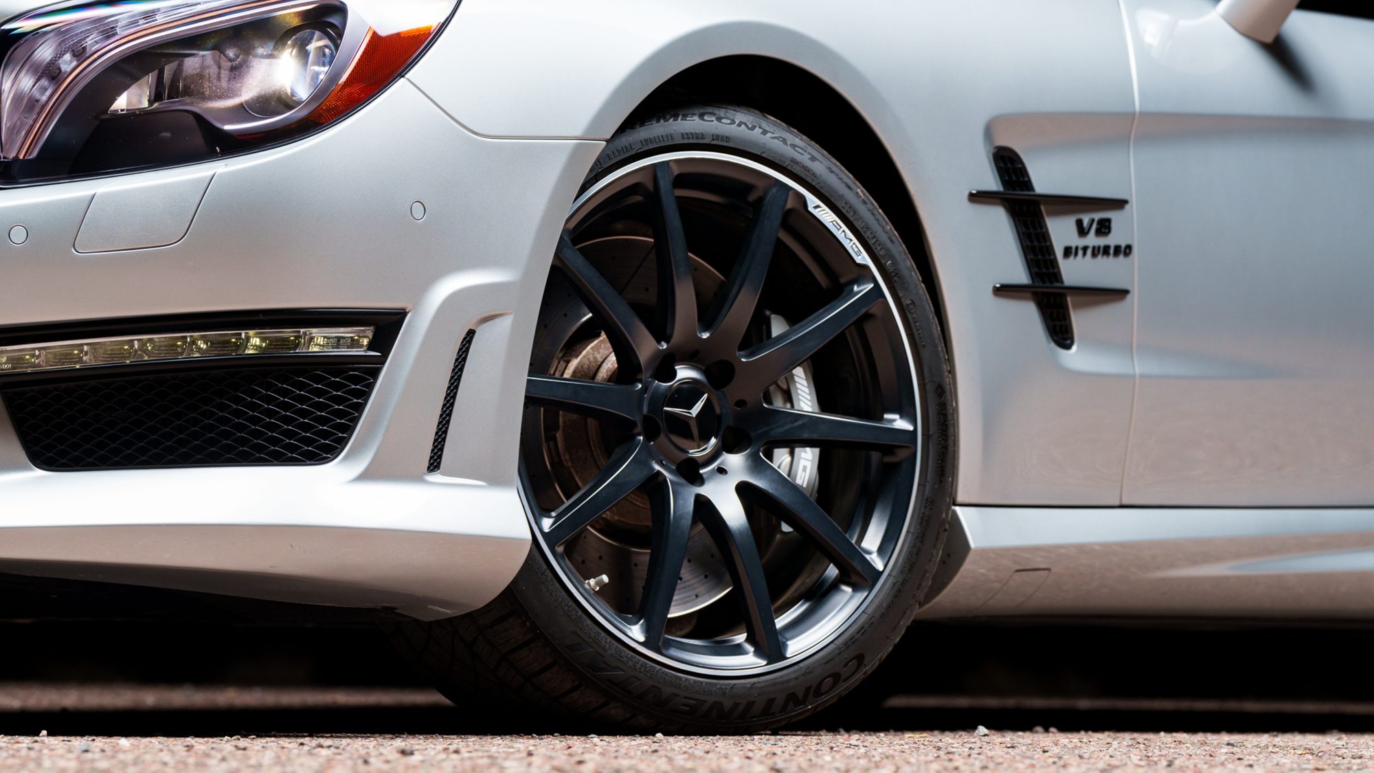 Close view of a Mercedes-Benz SL 63 AMG's dark multi-spoke wheel, headlight and front fender, with a V8 Biturbo badge on the fender vent