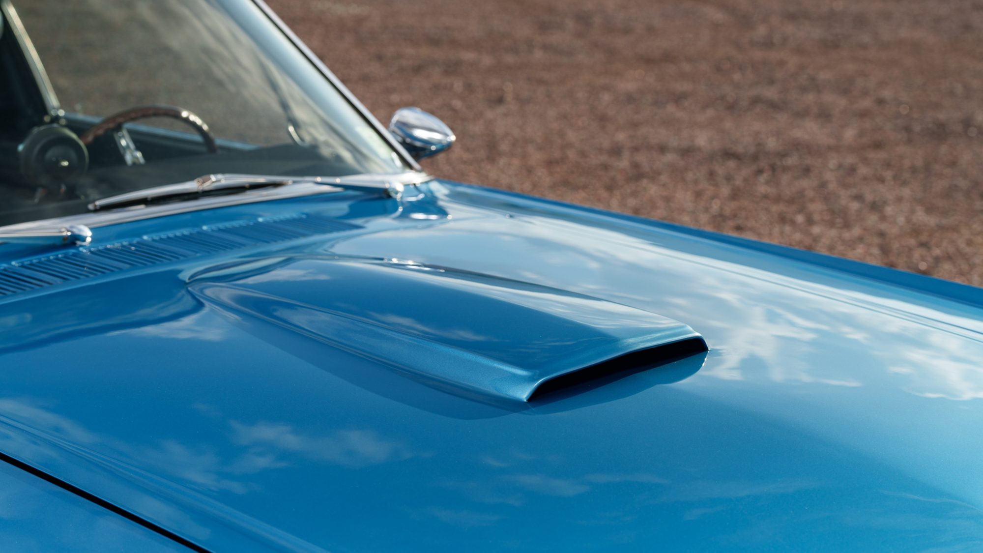 The scoop on the blue hood of a Shelby GT350, with the cowl vent, wipers and a chrome mirror beyond it