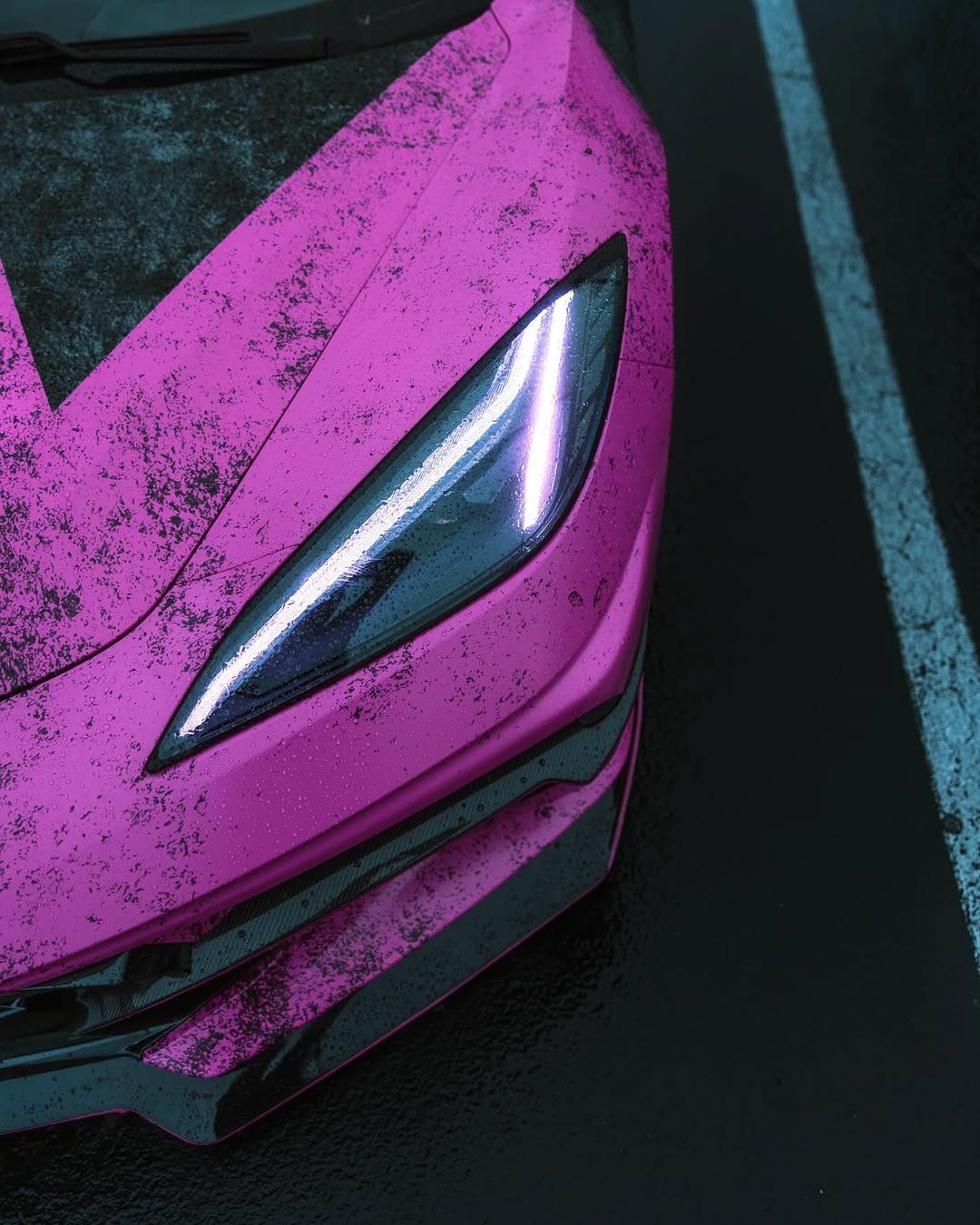 An overhead close-up of the Corvette's angular LED headlight, lit, set in the pink and black distressed wrap and beaded with rain