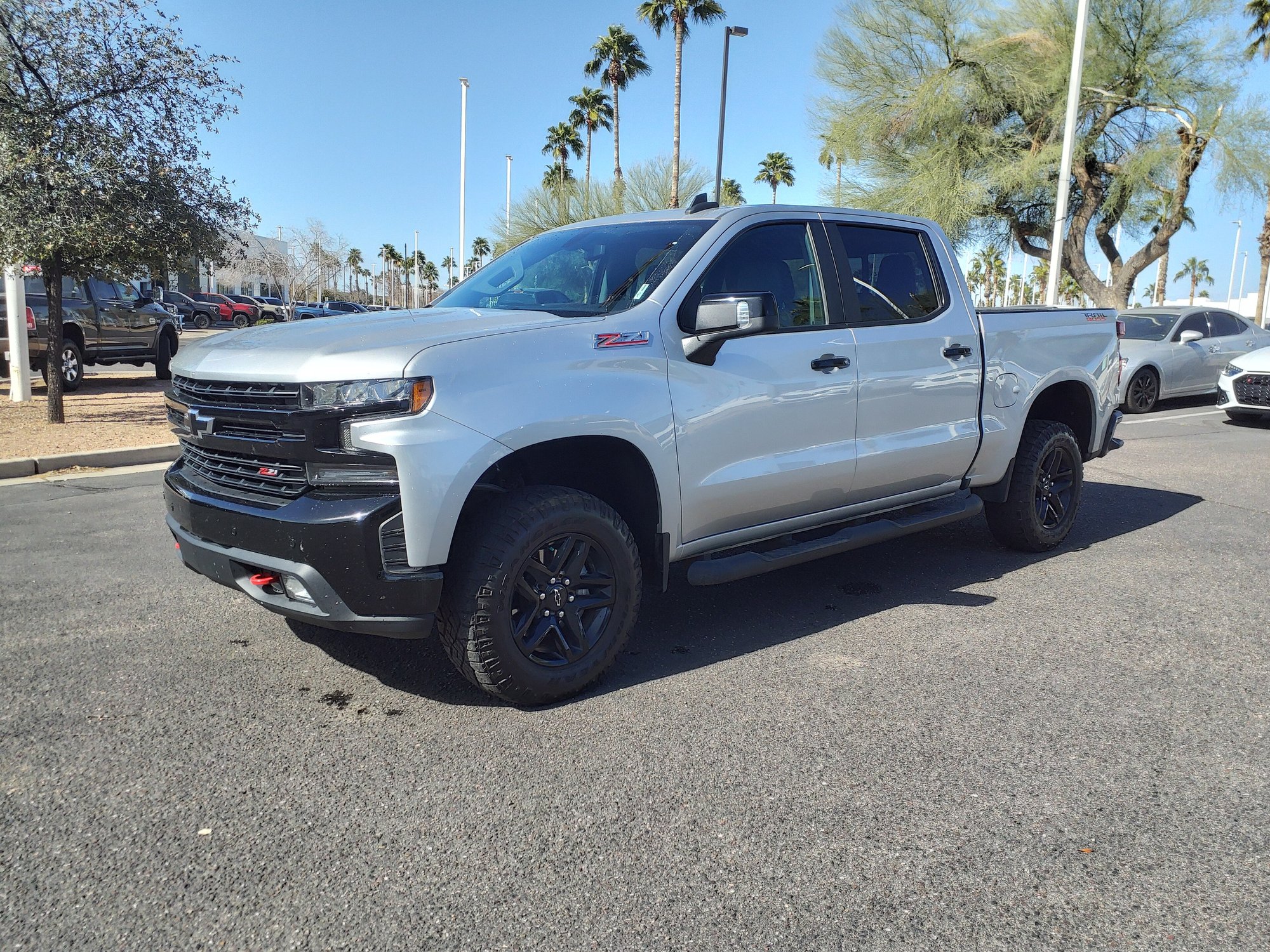 A silver Chevrolet Silverado crew-cab pickup in a parking lot, seen from the front left, with a black side step bar running along the bottom of the doors