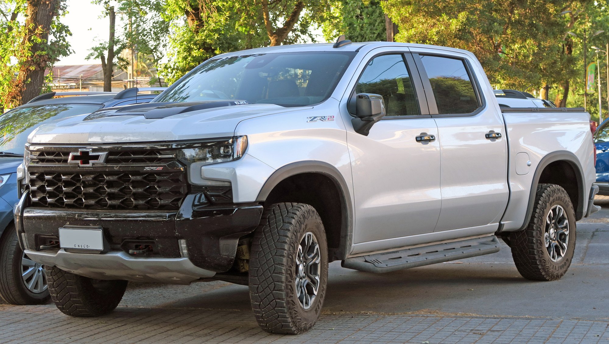 A silver Chevrolet Silverado ZR2 pickup parked on a brick-paved lot, seen from the front left, with large tires filling the wheel arches