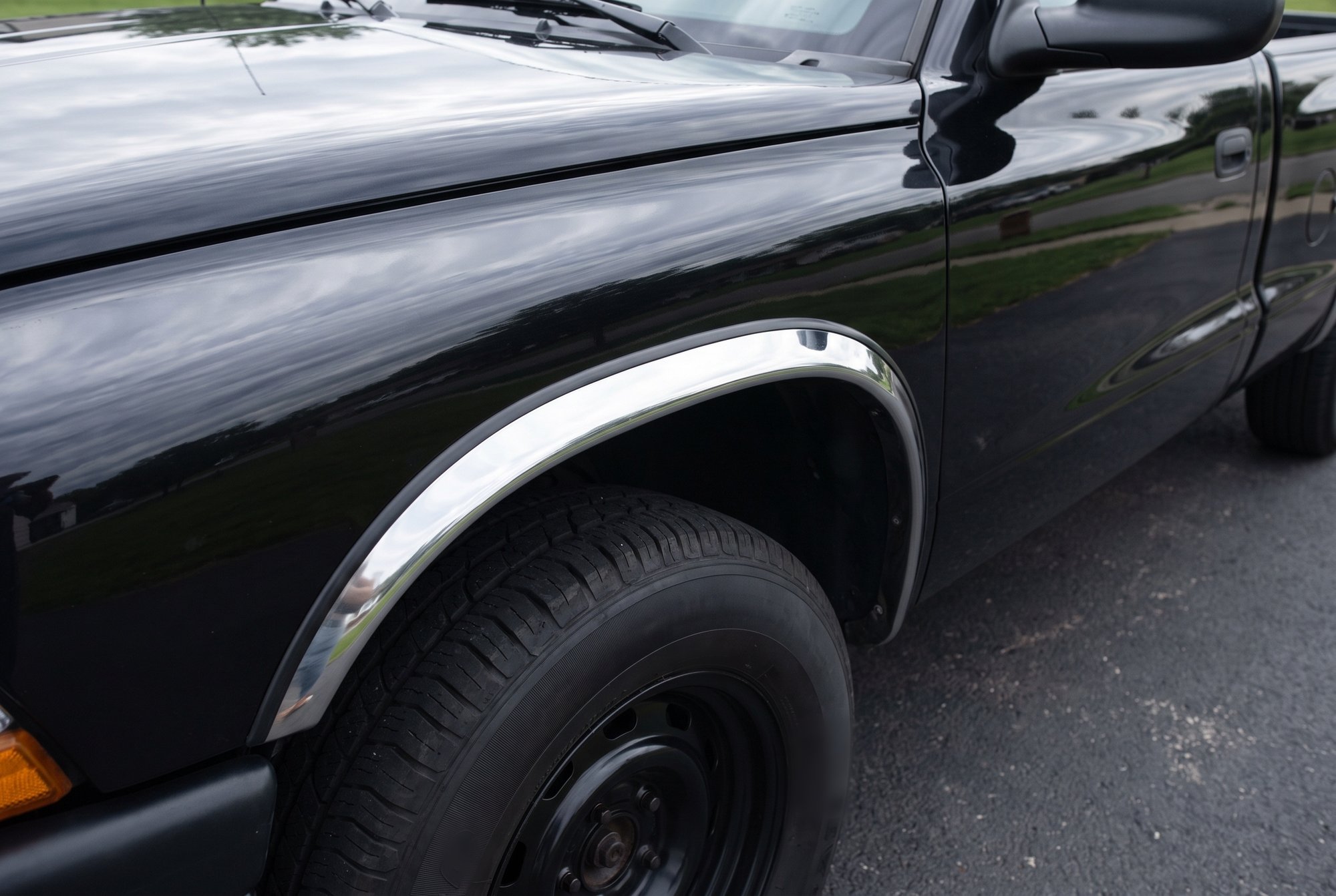 The front wheel arch of a black pickup, with a polished stainless steel trim strip along the fender lip