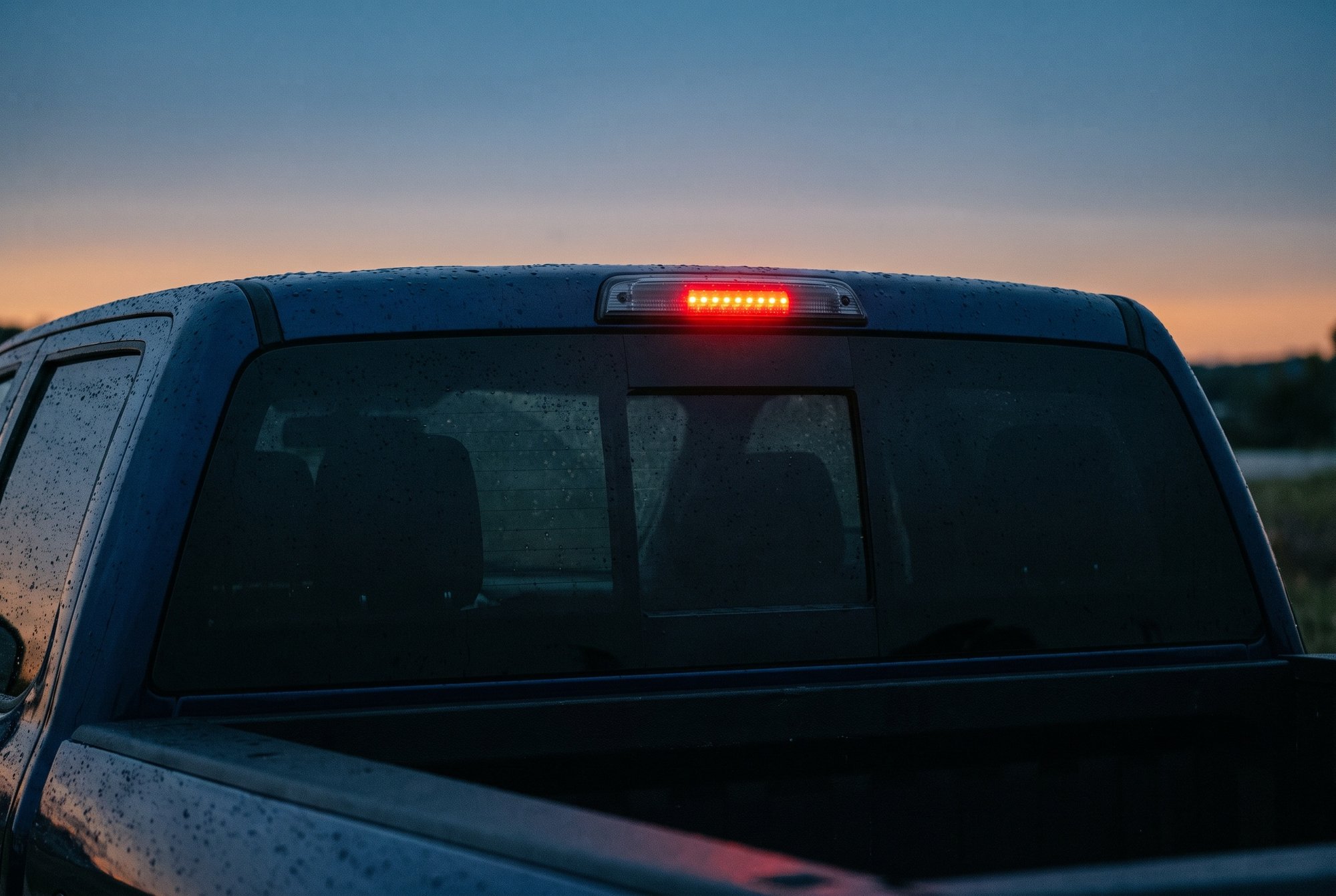 The back of a dark blue pickup cab at dusk, with an LED third brake light glowing red above the rear window
