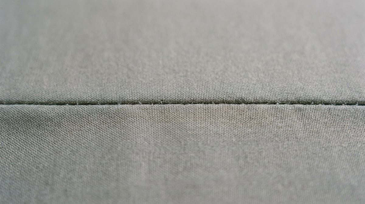 Close-up of a grey woven car cover fabric with a single stitched seam running across the frame