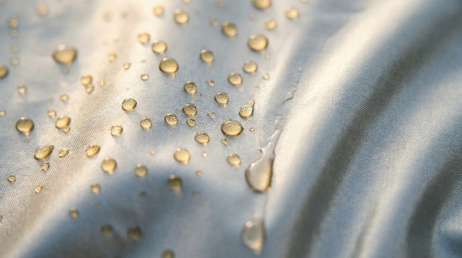 Close-up of water beads on a silver car cover fabric, with one bead running down a fold