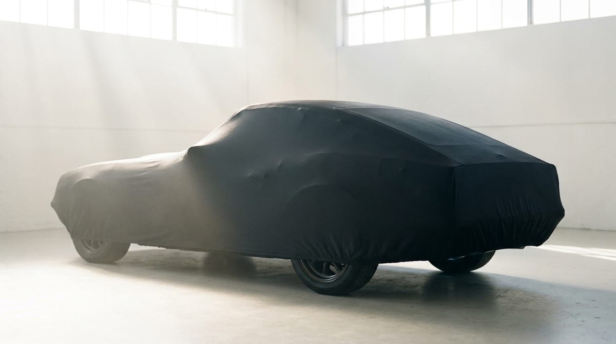 A sports car under a black satin cover in a bright, empty room with tall windows.